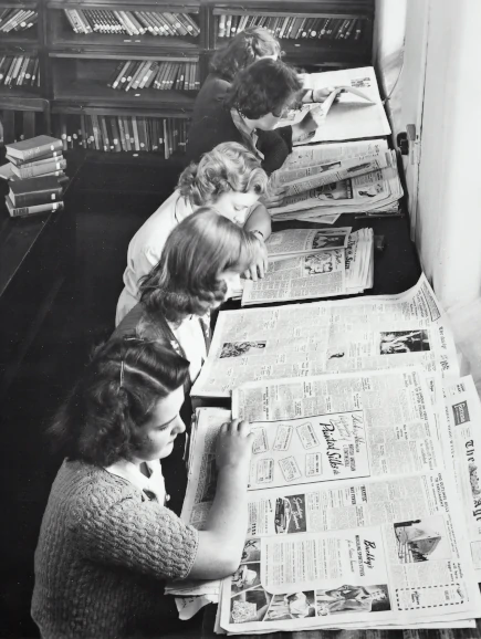 5 filles alignées concentrées qui lisent des journaux, image en noir et blanc | itinerares