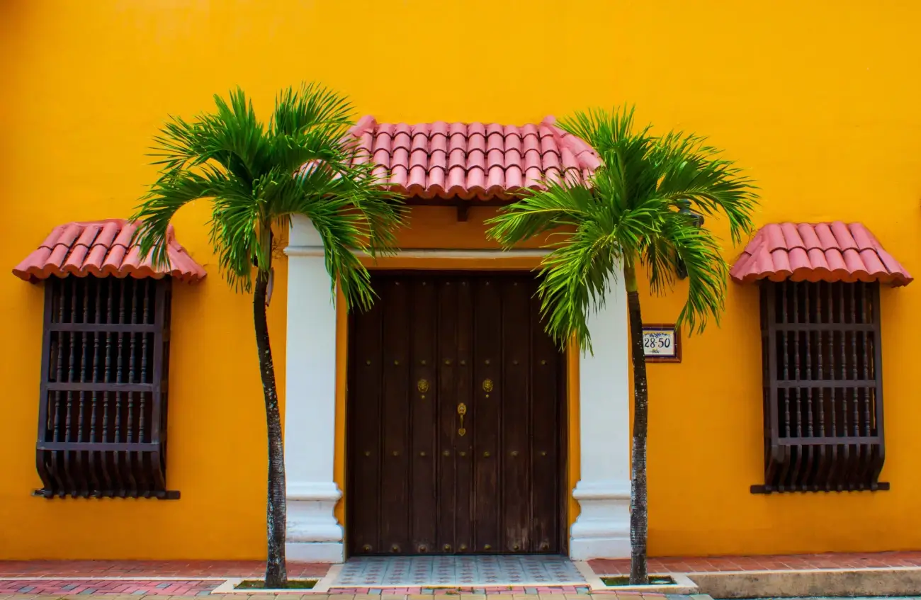 Façade jaune avec une porte marron entourée de 2 palmiers vers | itinerares