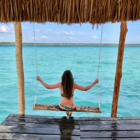 fille sur une balançoire en bois devant une lagune bleue turquoise | itinerares